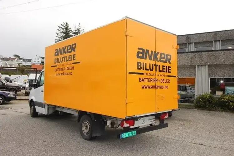 En gul leiebil fra Anker Bilutleie med logo og tekst på siden, parkert på en gate.