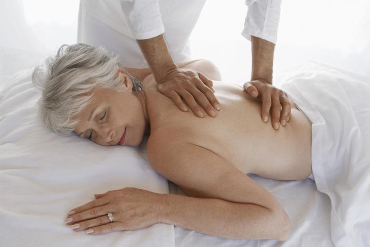 En eldre kvinne får massasje på en massasjebenken, med en terapeut som masserer ryggen hennes.