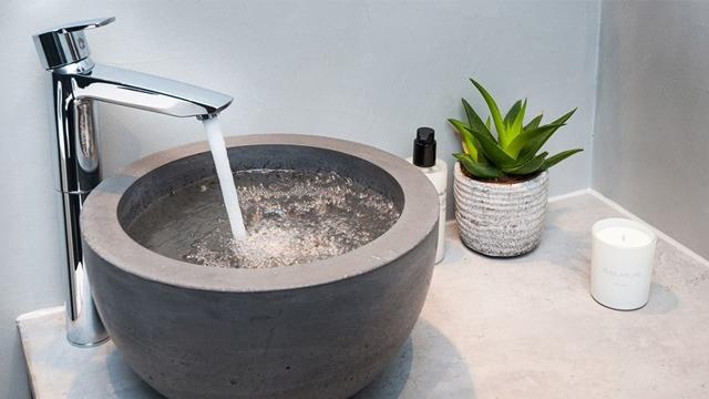 Et moderne baderom med en rund betongvask, kran som renner, en grønn plante og et stearinlys.
