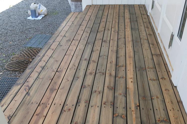 Nybehandlet treterrasse med jevne planker, plassert foran en bygning.