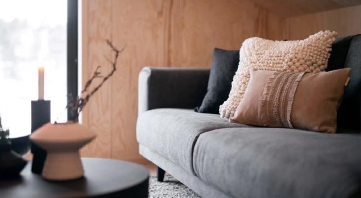 Moderne stue med en grå sofa, puter i forskjellige farger og en svart bord med dekorative gjenstander.