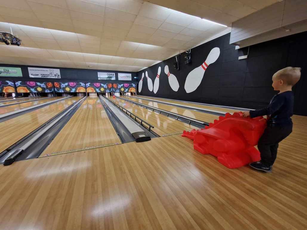Liten gutt som drar en rød duk på bowlingbane med flere bowlingkjegler i bakgrunnen.