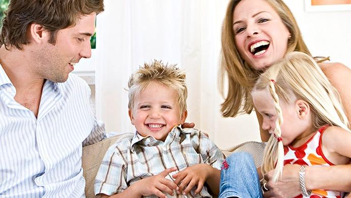 En glad familie sitter sammen i stuen, med to barn som smiler og leker med foreldrene.