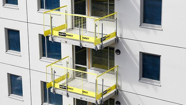 To balkonger med gule rekkverk på en moderne bygning med hvit fasade og vinduer.