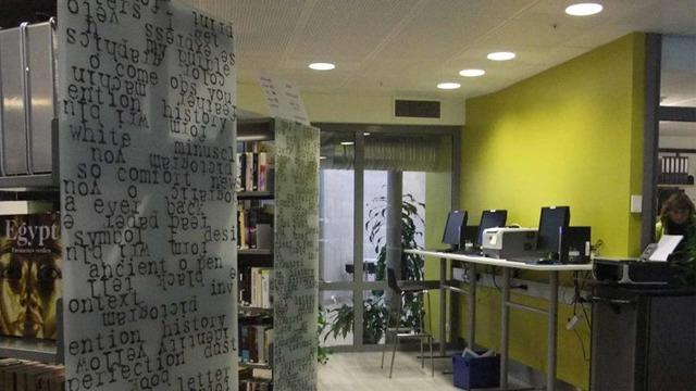 Moderne bibliotekinnredning med datamaskiner, bøker og en grønn vegg dekorert med tekst.