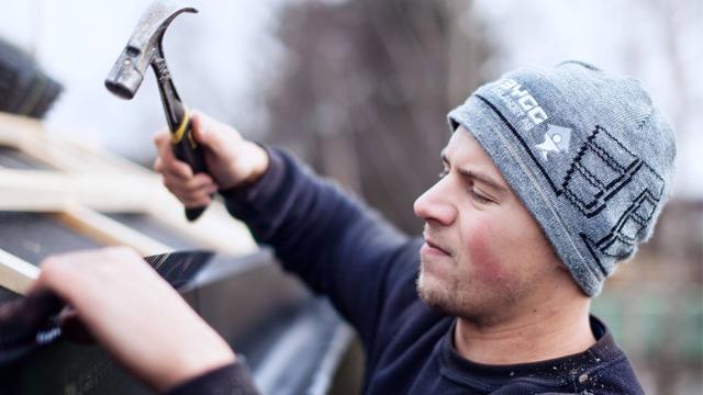 En håndverker bruker en hammer til å feste takplater på et tak.