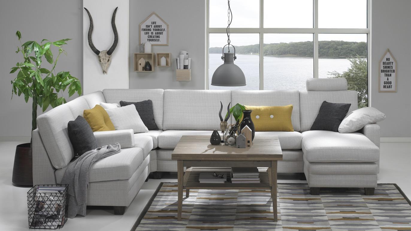 Moderne stue med hvit sofa, trekaffebord, dekorative puter og planter, med utsikt over vannet.