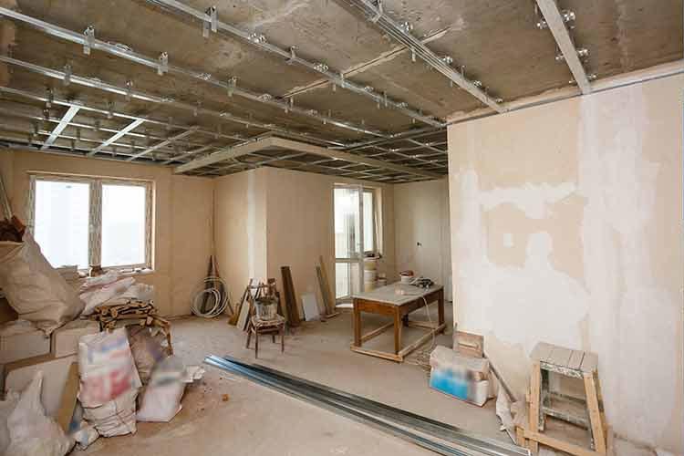 Rom i renovering med uferdige vegger, byggeutstyr og møbler stablet rundt.