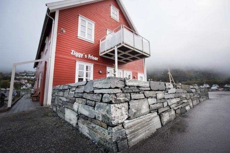 Rødt hus med balkong og steinmur, del av Zügger's frister, omgitt av tåke og landskap.