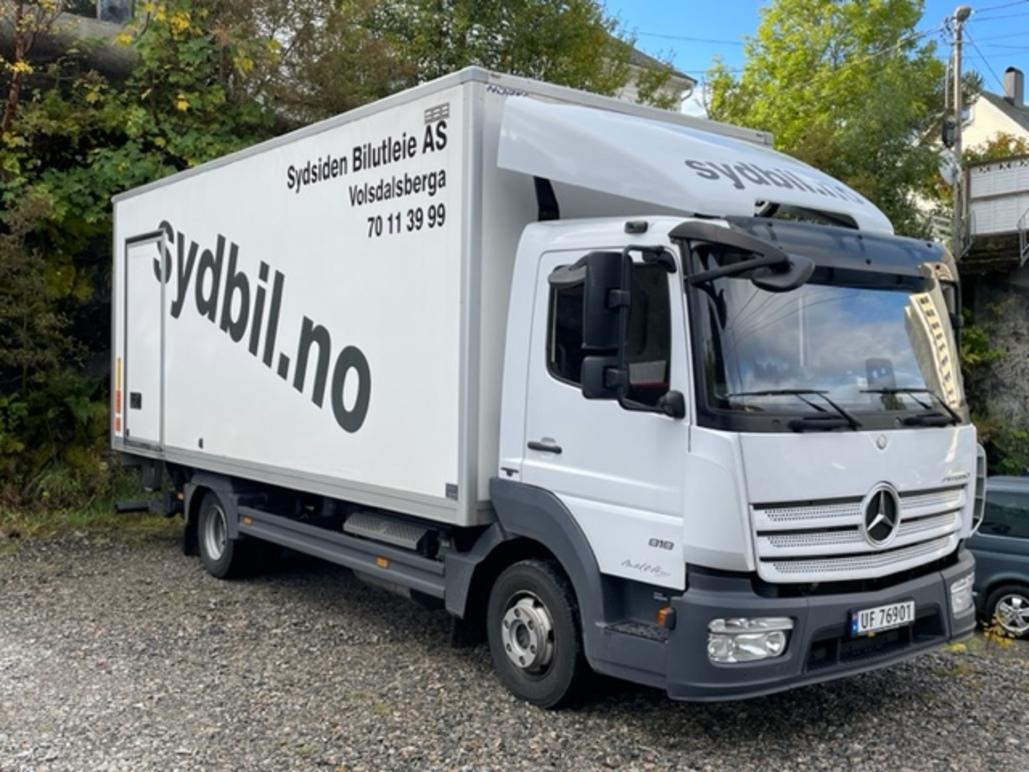 En lastebil fra Sydbil Bilutleie AS parkert på en grusvei med grønt landskap i bakgrunnen.