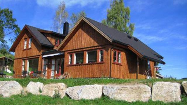 En koselig hytte i tre med skråtak, plassert på en grønn plen med store steiner foran.