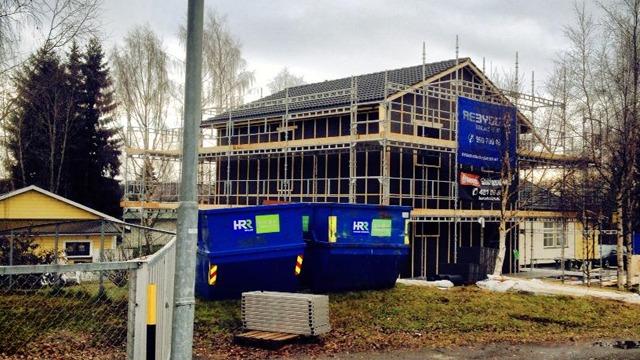 Nybygg med stillas og byggecontainere foran, omringet av trær og en annen bygning i bakgrunnen.