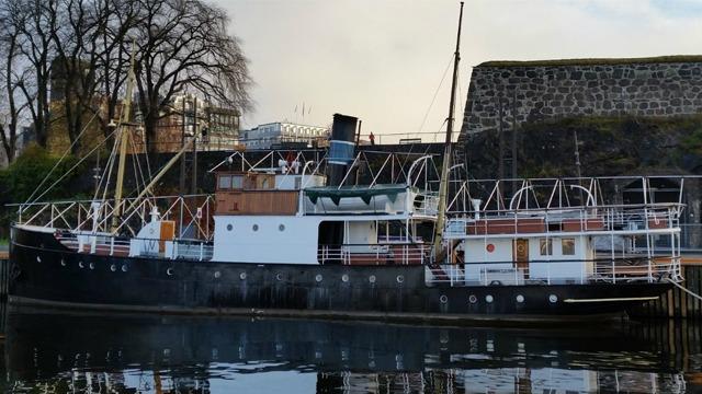 Et gammelt skip ligger ved kaien, med en svart og hvit fargekombinasjon og en stor skorstein.