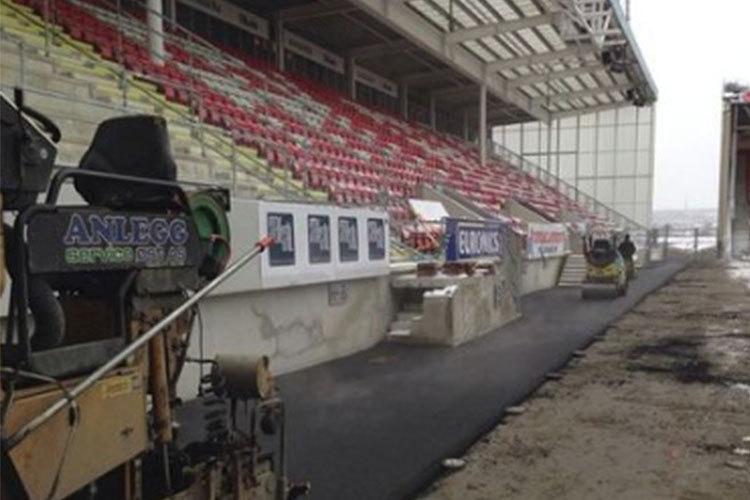Asfaltering av en stadion med tomme seter og reklameplakater langs tribunen.