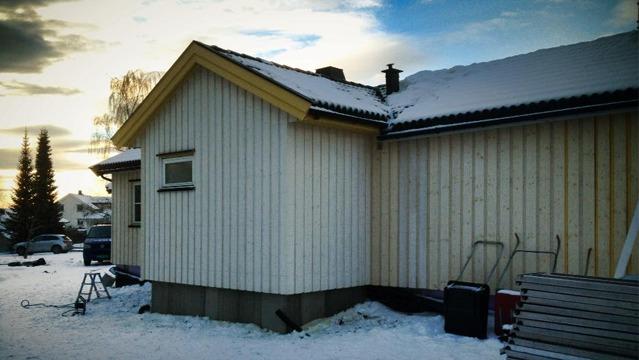En snødekt enebolig med trepanel og skråtak, beliggende i et vinterlandskap.