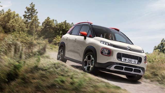 En hvit SUV fra Citroën kjører på en grusvei omringet av trær og natur.