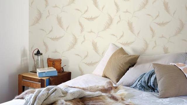 Soverom med veggdekor i beige blader, en seng med puter og et nattbord med bøker og lampe.