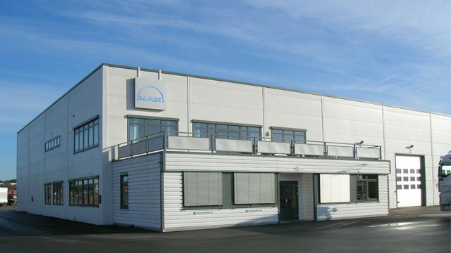 Moderne kontorbygg med store vinduer og en lys fasade, plassert under en klar blå himmel.