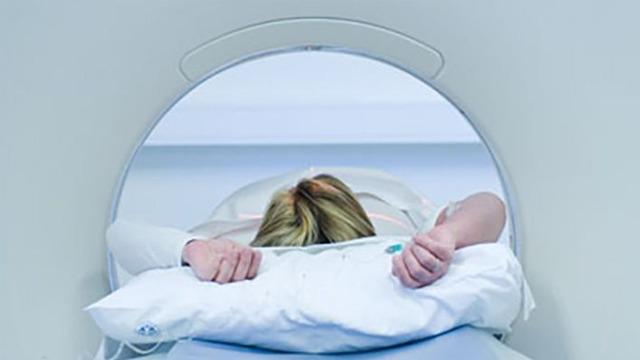 En pasient ligger på en CT-skanner med hodet inne i maskinen, armene strukket ut på en pute.