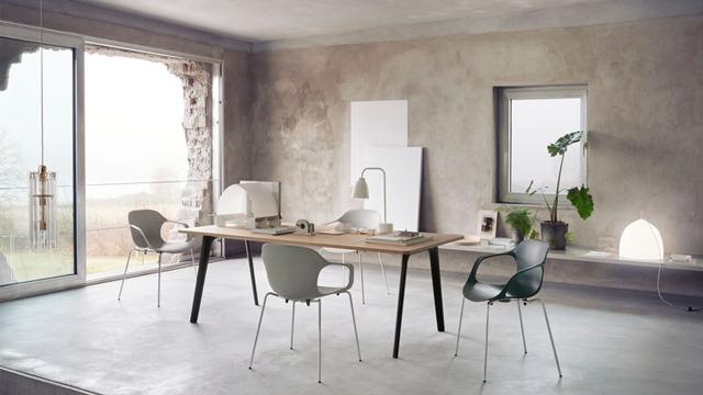 Moderne kontorinnredning med et stort bord, stoler i forskjellige farger og store vinduer som slipper inn naturlig lys.