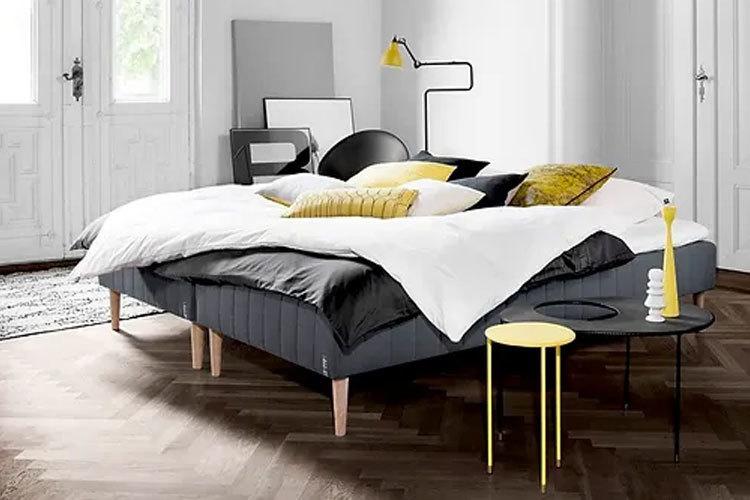 Moderne soverom med en stor seng, puter, sengeteppe og et lite bord med en lampe.