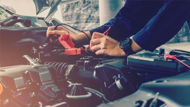 En mekaniker som tester bilbatteriet med måleinstrumenter under bilens motorlokk.