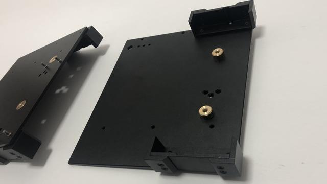 Svart metallplate med festeskruer, brukt til montering av elektroniske komponenter.