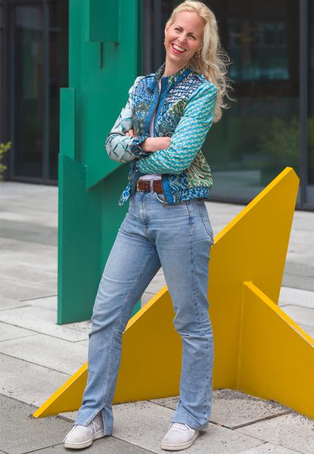 Kvinne med langt, lyst hår iført en fargerik jakke og jeans, står foran en stor, gul stjerneformet skulptur.