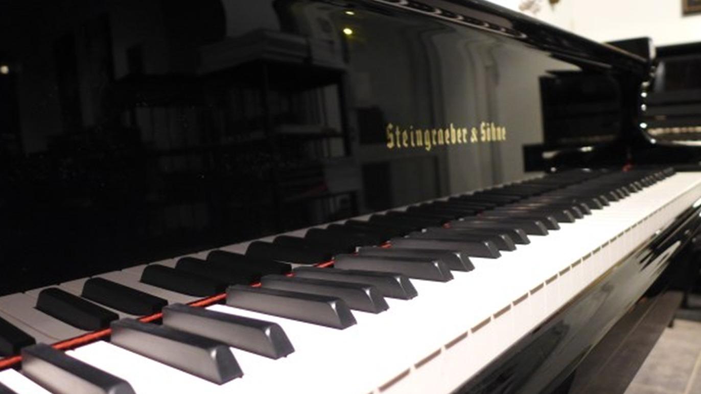 Et nærbilde av et svart piano med hvite og svarte tangenter, med navnet "Steinway & Sons" synlig.