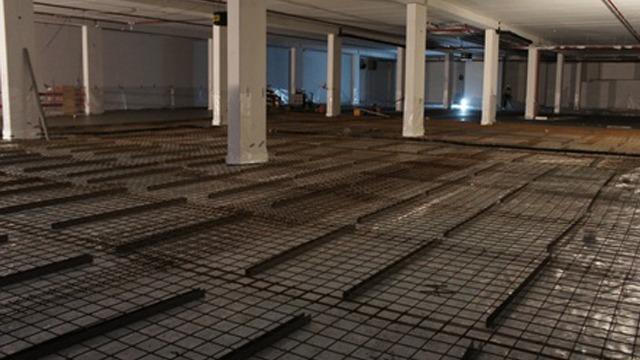 Bilde av et stort, tomt rom med betonggulv og stålstenger lagt ut for konstruksjon.