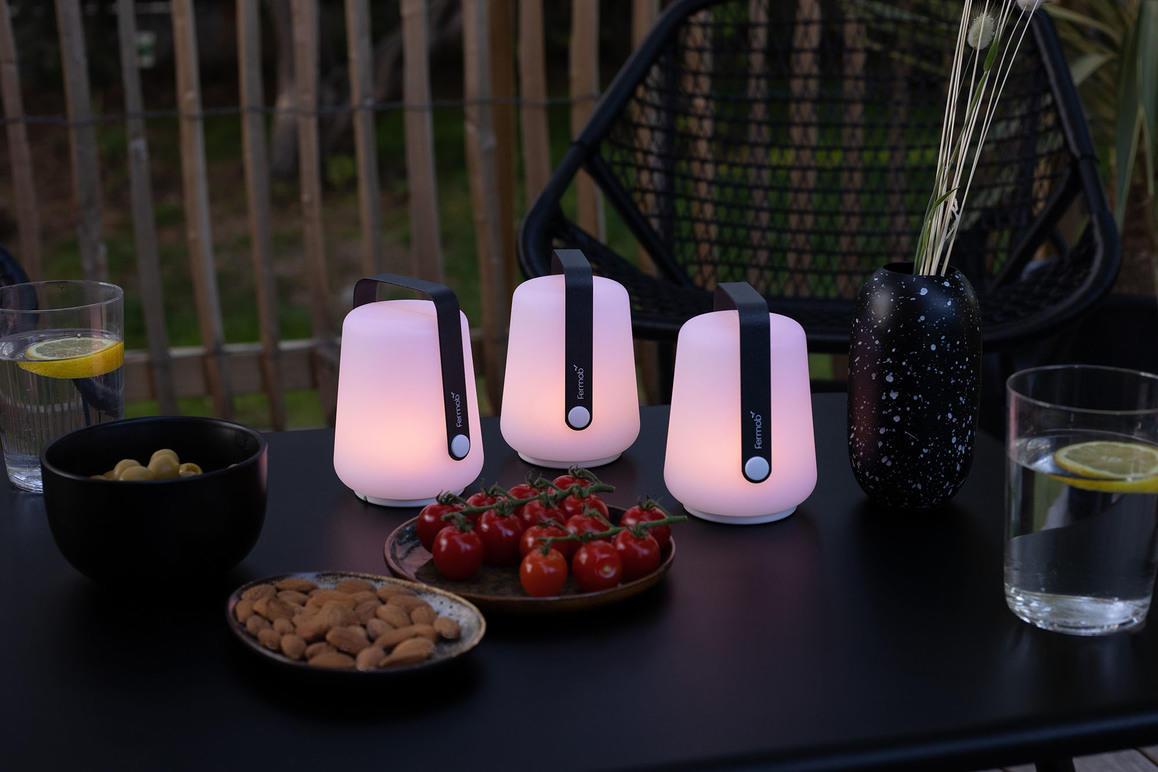 Tre stilige lamper med mykt lys står på et bord med snacks og drikke, omgitt av en koselig uteplass.