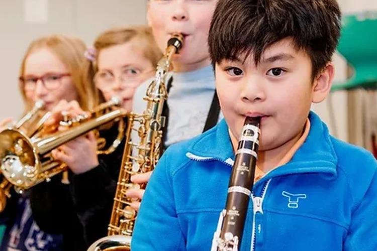 En gutt spiller klarinett foran en gruppe barn som spiller messingblåsere.