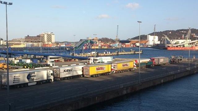 Havnen med lastebiler parkert ved kaien, skip i bakgrunnen og klar himmel.