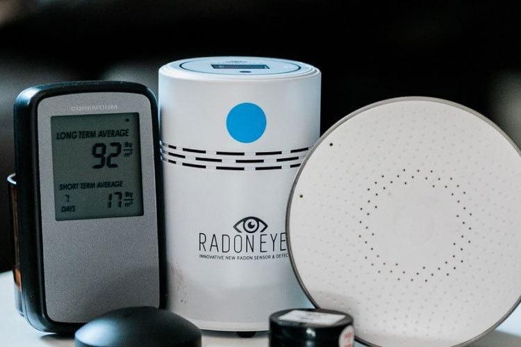 Bilde av radonmåler og tilbehør, inkludert en digital skjerm som viser radonnivåer og en sensor.