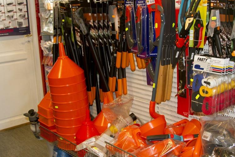 En hylle med oransje trakt og hageverktøy som spader, rake og klippere i en jernvarebutikk.