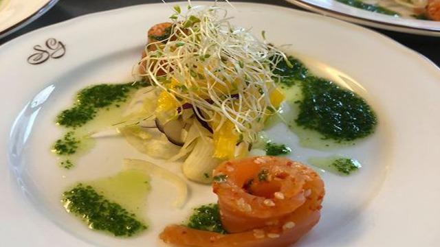 En elegant tallerken med reker, spirer, mango og urtesaus, dekorert med grønne urter.