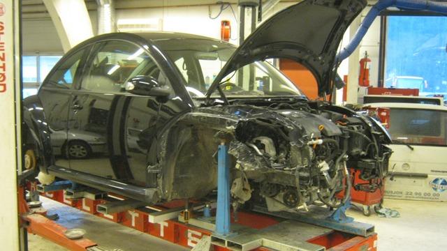 En svart bil med åpen motorlokk står på en heis i et verksted, delvis demontert.