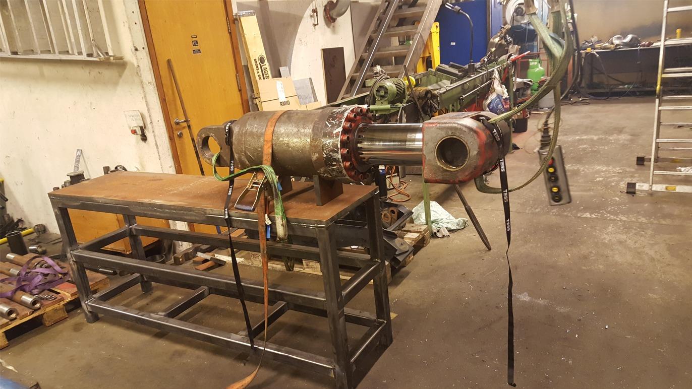 En stor motor på en arbeidsbenk i et verksted, med ledninger og verktøy rundt.