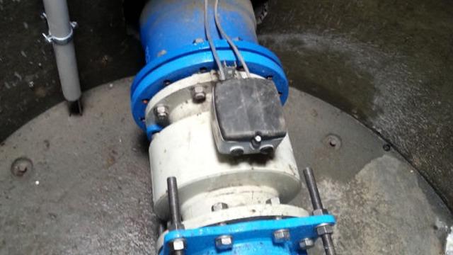 En blå og hvit ventil med elektrisk sensor i en betongbrønn.
