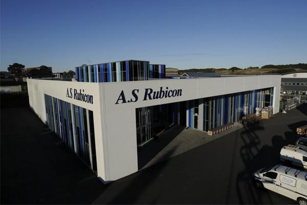 Moderne bygning med navnet A.S Rubicon, med solcellepaneler og glassfasade, beliggende i et industriområde.