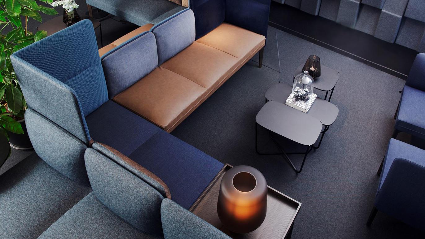 Moderne stue med en u-formet sofa i blå og brun farge, et svart bord og en dekorativ lampe.