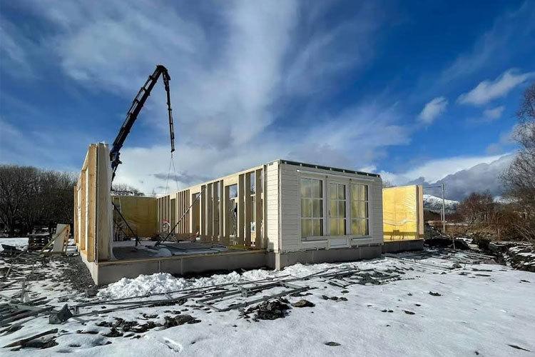 Bygging av moderne hus med betongpumpe, snø og blå himmel i bakgrunnen.