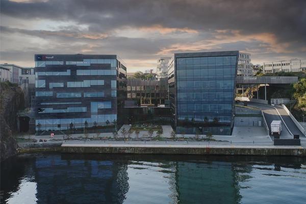 Moderne bygninger ved vannkanten med speilende glassfasader og en dramatisk himmel i bakgrunnen.