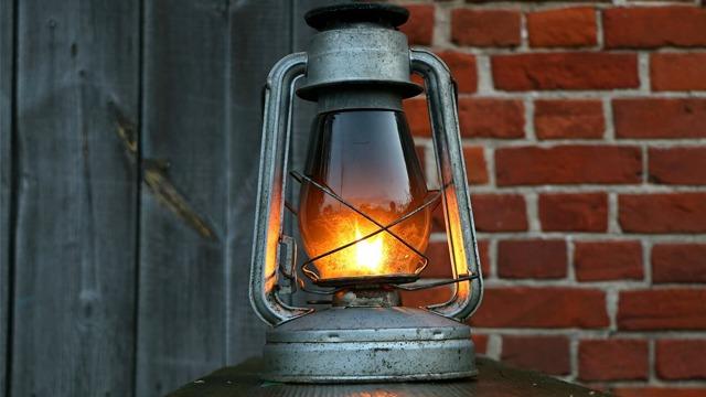 En gammel lampe med glass og metall, som lyser opp mot en rød murvegg.