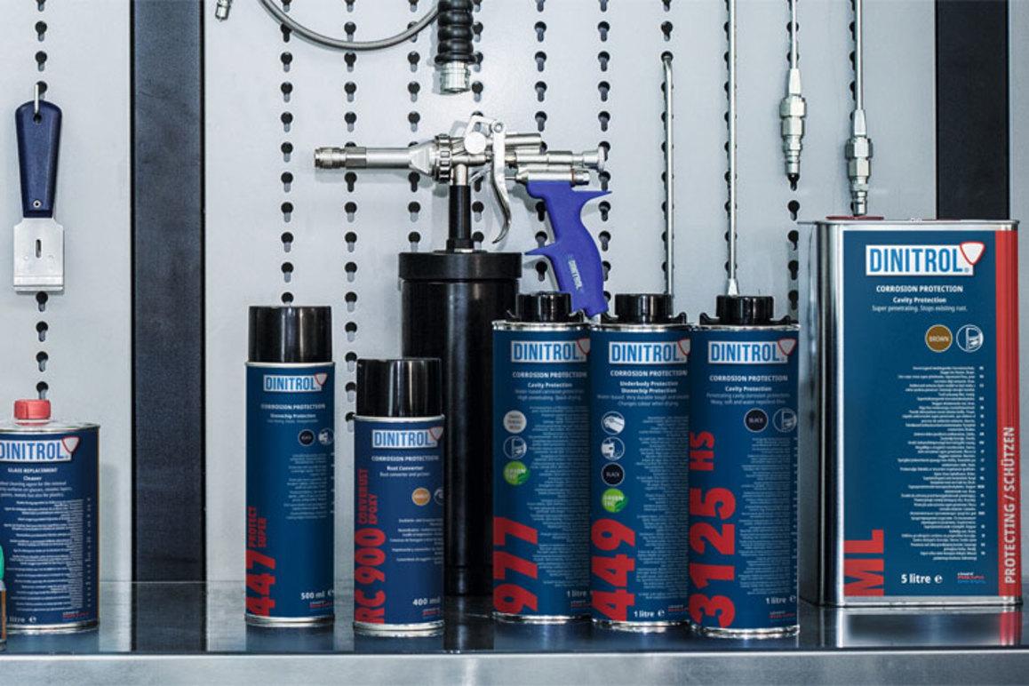 Bilde av DINITROL produkter på en verkstedvegg, inkludert spraybokser og en sprøytepistol.