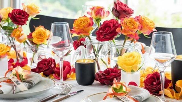 En elegant borddekorasjon med røde, gule og oransje roser, glass og servise til en festlig middag.