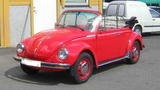 En rød Volkswagen boble cabriolet parkert på en gate med andre biler i bakgrunnen.