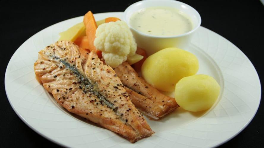 Grillet laks med poteter, blomkål og grønnsaker, servert med hvit saus i en skål.