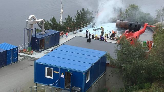 Trening på en redningsøvelse med helikopter og røyk på en plattform ved vannet. Flere personer deltar i øvelsen.