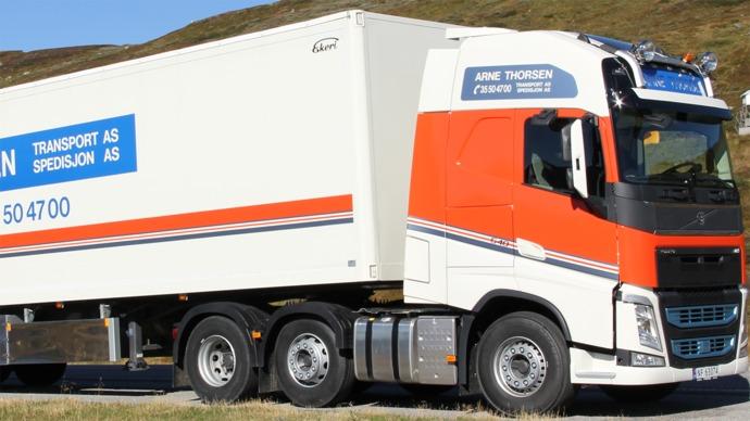 En stor lastebil med tilhenger, merket med "A. Thoresen Transport AS", står på en vei i et fjellområde.